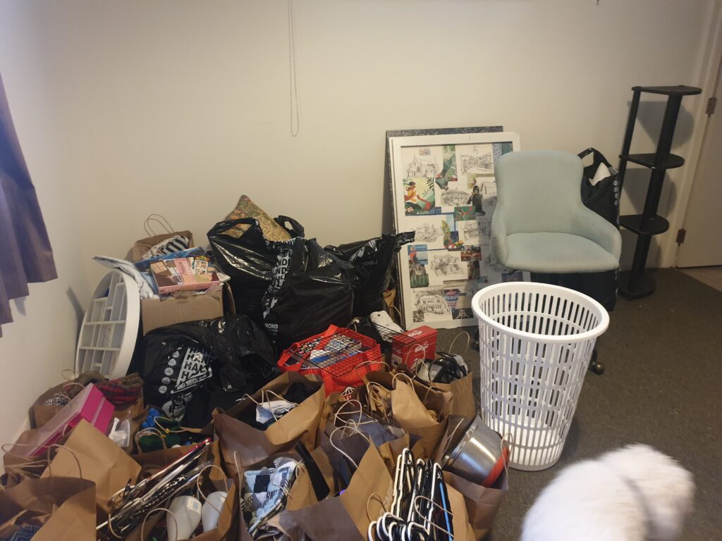A lot of bags filled with household items on the floor of a room, and some pieces of furniture. 