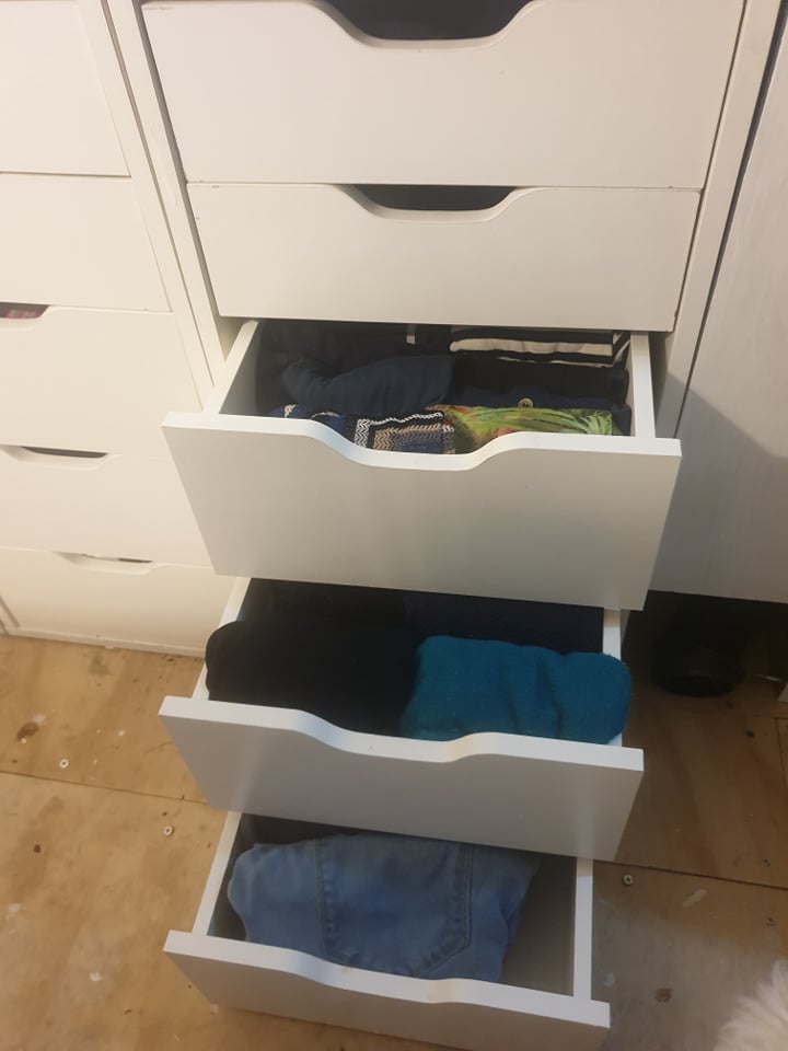 A set of white drawers, with three of the drawers open showing folded clothes. 